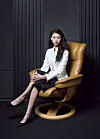 Woman seated in a tan leather chair in a dark studio setting.