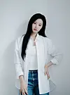 Woman posing in a white shirt, white top, and blue jeans against a gray background.