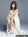 Studio portrait of a woman in a white dress and sneakers seated against a gray background.