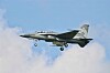 A fighter jet flying with landing gear down against a cloudy sky.