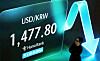 Screen in Hana Bank dealing room shows USD/KRW rate 1,477.80 with a blue downward arrow graphic.
