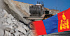 Mining machinery operates on a rocky slope beside a large haul truck and piles of excavated stone.