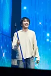 A singer stands on a blue stage holding a microphone stand.