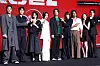 Cast and crew posing on stage in front of a red backdrop at a Disney+ series press event.