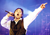 Shin Hae-chul performs onstage with a microphone, arm raised under blue and purple lights.