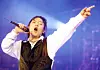 Shin Hae-chul performs onstage with a microphone, arm raised under blue and purple lights.