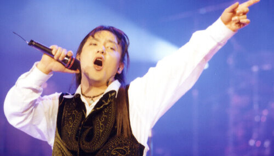 Shin Hae-chul performs onstage with a microphone, arm raised under blue and purple lights.