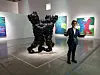 Visitor standing next to a shiny black abstract sculpture in an art gallery.