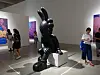 A large black sculpture stands in a museum gallery as visitors look around nearby.