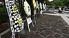 White floral wreaths with condolence ribbons line a stone path at Bongha Village during a memorial event.