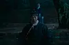 Person in traditional clothing standing in dark water near stone steps at night.
