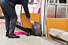 A person reaches down to pick up a bag left on the floor of a train.