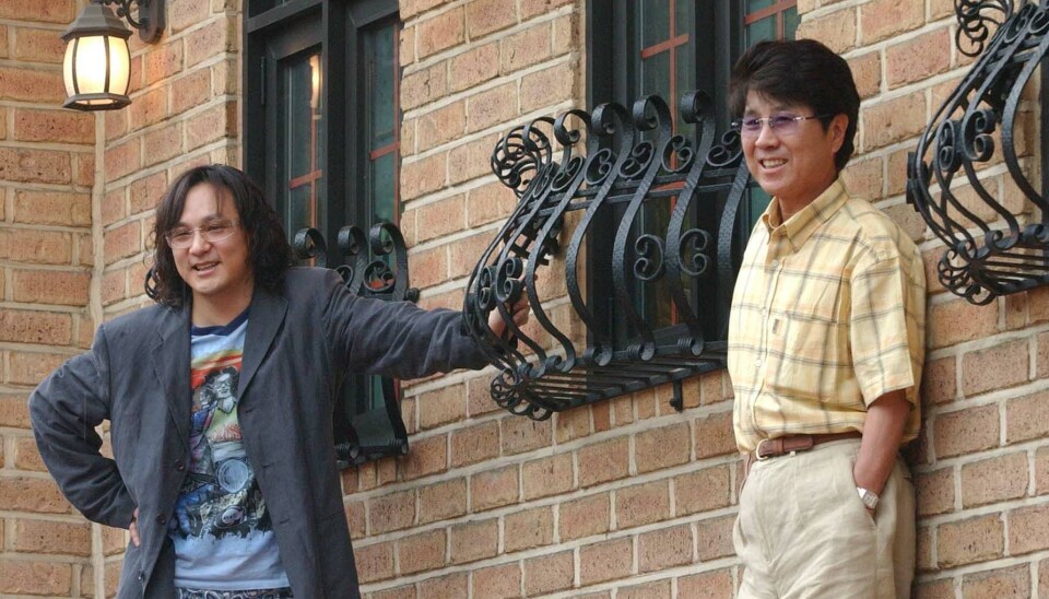 Two men stand by a brick building with iron window grilles and wall lanterns.