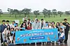 A large group holds a blue banner while posing on a wet path in a grassy park.