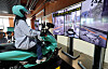 A rider sits on a scooter simulator facing large screens during VR safety training at Baemin Riders School.
