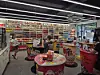 People browsing inside a brightly lit snack store with colorful product displays and red tables.