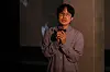 Hong Jin-hwon holding a microphone on a dimly lit stage.
