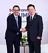 Two men in suits shake hands in front of a San Francisco summit backdrop.