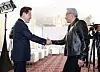 Two men shake hands in a bright room as photographers capture the moment.