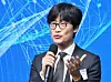 Lee Hae-jin speaks into a microphone at an AI summit with a blue digital background.