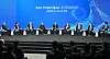 Panel of executives and officials seated onstage at the San Francisco AI Summit with a blue digital backdrop.