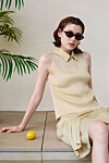 Woman in sunglasses seated on a ledge next to a lemon and a palm plant.