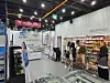 Shoppers browse products inside a supermarket aisle near a refrigerated display and promotional signs.
