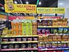Colorful snack packages arranged on a convenience store display beneath bright promotional signs.