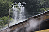 A drone sprays coating onto a sloped farm roof with mist rising in a wooded rural setting.