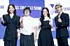 Four people stand before a branded event backdrop, smiling and giving thumbs-up gestures.