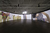 People inside a gallery surrounded by large colorful wall panels and artwork beneath a dark ceiling.
