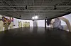 People inside a gallery surrounded by large colorful wall panels and artwork beneath a dark ceiling.