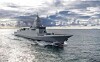 Grey naval destroyer sailing on open water beneath dramatic cloud cover.