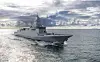 Grey naval destroyer sailing on open water beneath dramatic cloud cover.