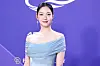 Actor in a light blue off-shoulder gown poses against a purple event backdrop.
