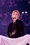 BTS member Jimin sings onstage in front of purple concert lights.