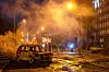 A burned car sits on a debris-strewn street with smoke rising after a missile attack in Kyiv.
