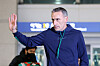 Paulo Bento raises his hand while walking through Incheon airport, with a blurred traveler and signage behind him.