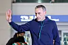 Paulo Bento raises his hand while walking through Incheon airport, with a blurred traveler and signage behind him.
