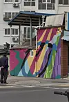 Colorful geometric mural on a street-side wall with apartment buildings behind it.