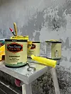 Paint cans, brushes, and a yellow caulk gun arranged on a metal cart near a gray wall.