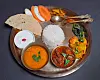 A metal tray with rice, curries, vegetables, flatbread, and sliced vegetables.
