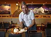 A server presents a plated meal inside a restaurant with mountain murals and warm lighting.