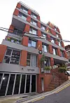 Red brick apartment building on a steep street with balconies and overhead power lines.