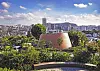 Copper-toned round building surrounded by trees with a city skyline and clouds in the background.