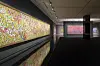 Bright abstract pixel-like artwork displayed along a gallery wall with reflections on a glossy floor.