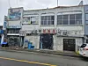 Old two-story building with Chinese signs beside a wet street and parked cars.