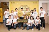 A group poses indoors in front of an International Beer Day 2026 backdrop with promotional signs.
