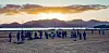 Groups of people on a rocky beach at sunset with mountains silhouetted behind them.
