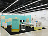 Museum exhibition space with turquoise panels, display tables, and informational wall text.